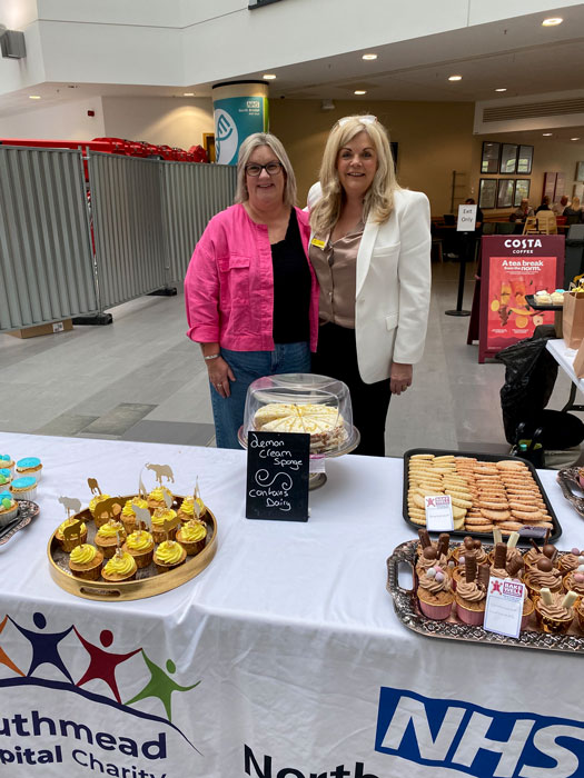 Photo of two ladies standing behind a table displaying cakes.